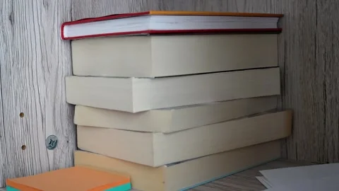 Stack of hardcover and paperback books leaning against wooden wall with colorful Stock Footage 345952761