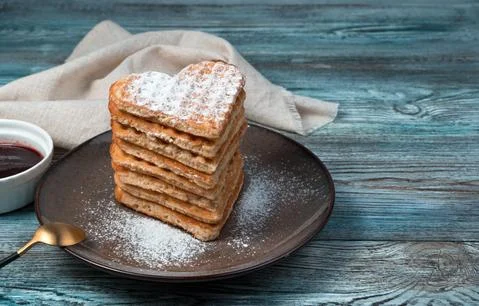 A stack of heart-shaped waffles sprinkled with powdered sugar on a wooden Stock Photos