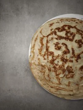 Stack of homemade crepes resting on a white plate on a gray surface copy space Stock Photos