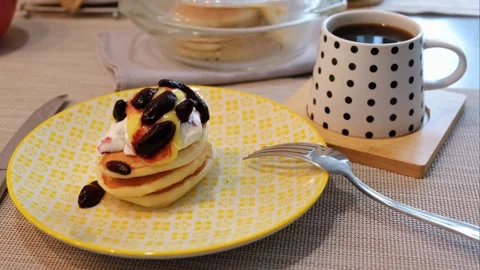 A stack of homemade pancakes on a yellow plate with sour cream, lemon curd, hone Stock Footage 304432913