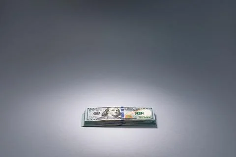 Stack of hundred dollar bills arranged on a gray background highlighting wealth Stock Photos