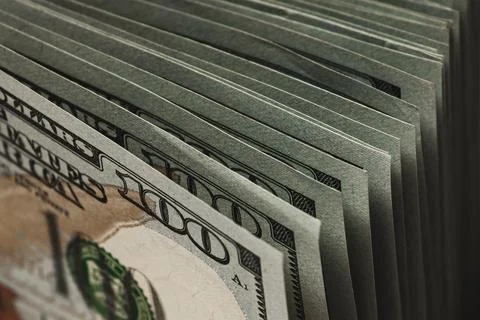 A stack of hundred-dollar bills edged on a dark background, top view. Stock Photos