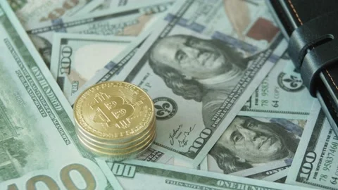 A stack of hundred-dollar bills with a gold bitcoin lying on top. A close-up of Stock Footage 221751264