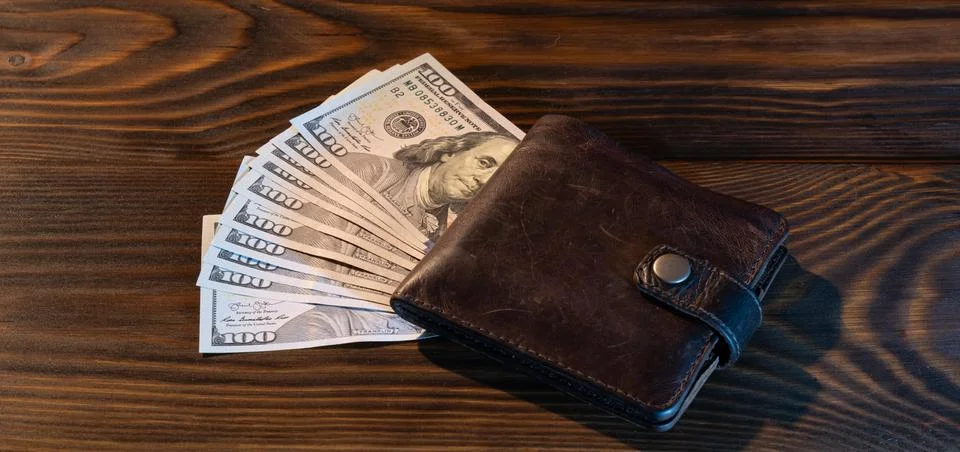 Stack of hundred dollar bills with leather wallet on noble wooden background Stock Photos