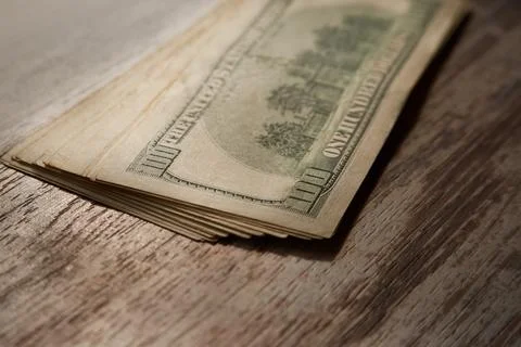 A stack of hundred-dollar bills lies on a wooden table, currency exchange, fi Stock Photos