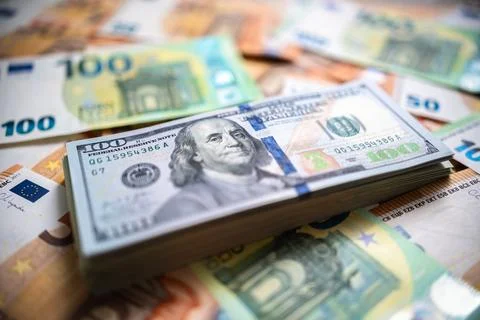 A stack of hundreds of American USD dollar bills is on top of euro banknotes Stock Photos