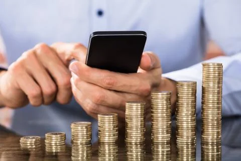 Stack Of Increasing Coins In Front Of The Businessman Using Smart Phone For C 库存照片