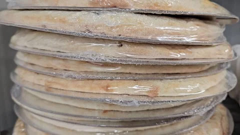 A stack of individually plastic wrapped, par baked pizza crusts Stock Footage 311591376