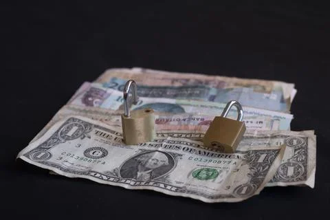 Stack of international currency bills secured with padlocks on black Stockfoto's