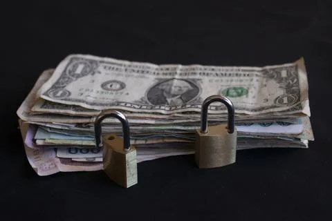 Stack of international currency bills secured with padlocks on black Stock Photos