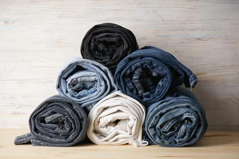 Stack of jeans in various shades, jeans are stacked on a light wooden backgro Foto stock