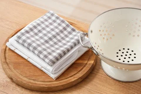 Stack of kitchen towels and white colander on wooden table Stock Photos