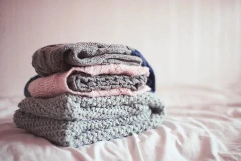 Stack of knitted clothes in bed close up. Winter season. Selective focus. Stock Photos