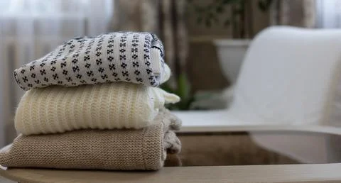 A stack of knitted clothes is folded on a table in the living room. Dismantling Stock Photos