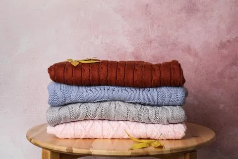 Stack of knitted clothes on wooden table against pink background. Cozy autumn 스톡 사진
