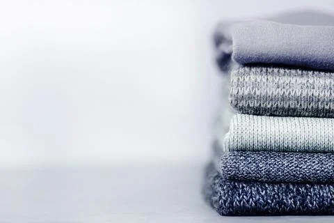 A stack of knitted jumpers and sweaters on a gray concrete blurry background. Stock Photos