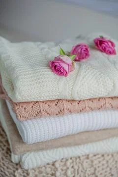 A stack of knitted sweaters, roses. Women's sweaters lie on the ottoman. Co.. Stock Photos