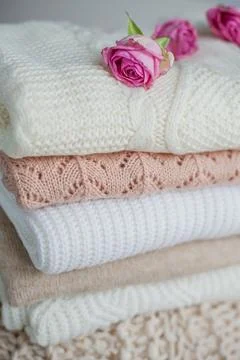 A stack of knitted sweaters, roses. Women's sweaters lie on the ottoman. Co.. Stock Photos