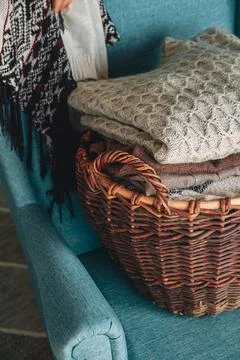 Stack of knitted sweaters on wicker basket on the armchair Stock Photos