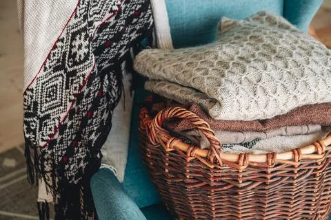 Stack of knitted sweaters on wicker basket on the armchair Stock Photos