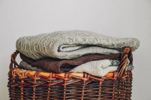 Stack of knitted sweaters on wicker basket. Stock Photos