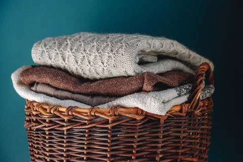 Stack of knitted sweaters on wicker basket. Stock Photos