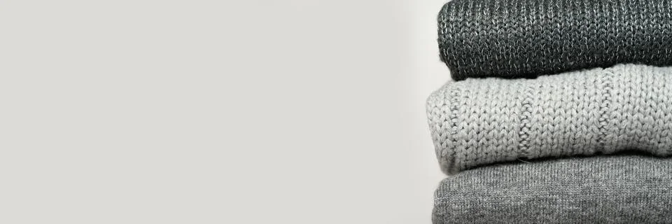 A stack of knitted winter sweaters in several shades of gray on gray backgrou Stock Photos