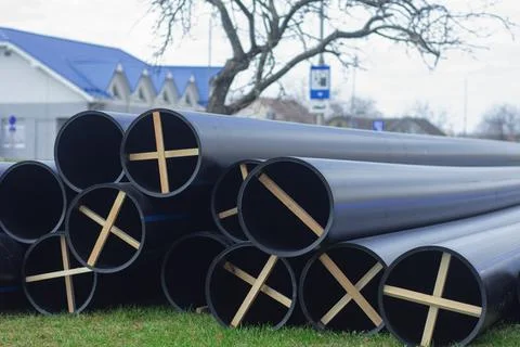 Stack of large black pipes for water mains with blue stripes, rests on a gras Stock Photos