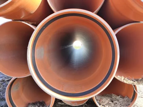 Stack of large orange industrial pipes with sunlight at tunnel end Stock Photos