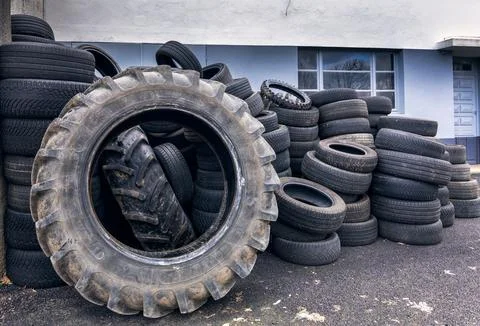 Stack of large used tractor and truck tires near an industrial wall surface Stock Photos
