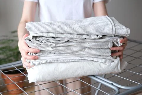 Stack of laundry and woman folding clean bedding and clothes Stock Photos
