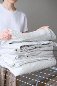 Stack of laundry and woman folding clean bedding and clothes Stock Photos