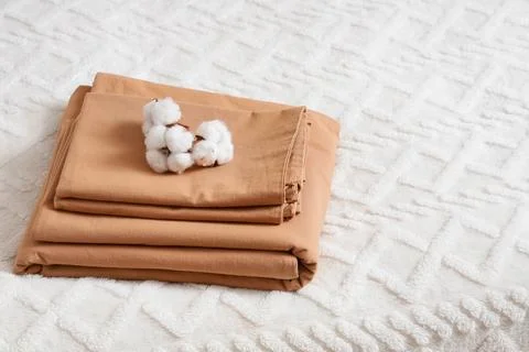 Stack of linen with cotton flowers on bed in room Fotos de archivo
