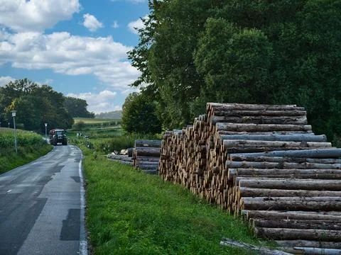 Stack of logs next to a road with a tractor approaching in the background o.. Stock-Fotos