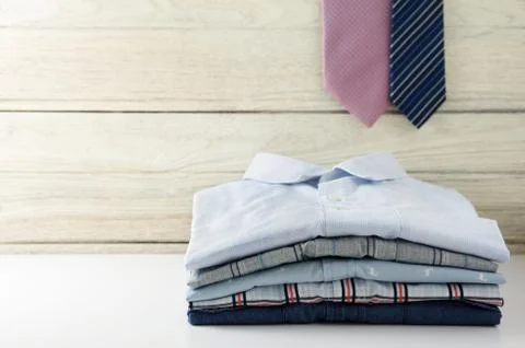Stack of men shirts and tie hanging with white wooden background Stock Photos