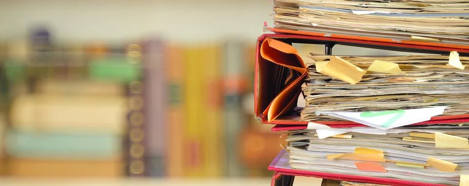 Stack of messy file folders with narrow depth of field, blurred bookshelf  .. Stock Photos