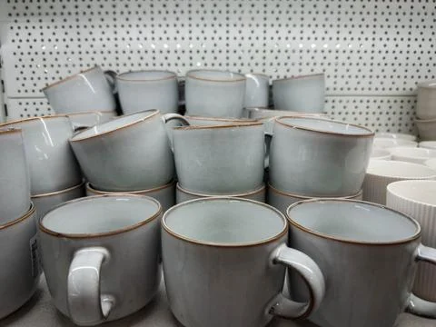 A stack of minimalist ceramic mugs displayed on a store shelf. Matte light-gr Stock Photos