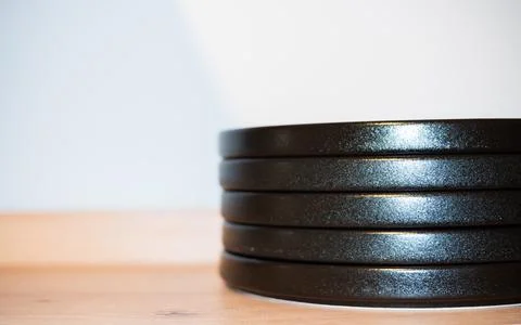 Stack of modern black ceramic plates on a wooden table surface with white wall Stock Photos
