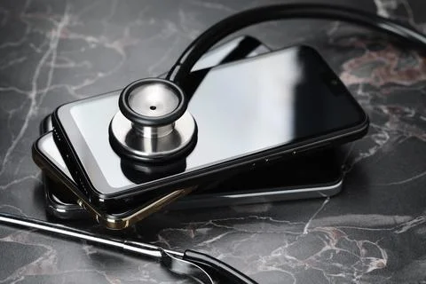 Stack of modern smartphones and stethoscope on black table Stock Photos