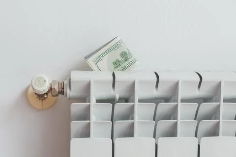 A stack of money dollars on a white battery heating radiator on a white wall, Stock Photos