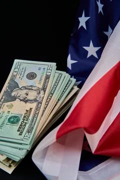 A stack of money is positioned alongside an American flag Stock Photos
