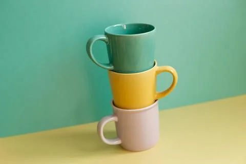 Stack of mug cups on yellow table. green wall background Stock Photos