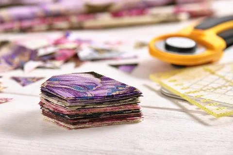 Stack of multi-colored pieces of fabric, ruler, cutting mat, rotary cutter Fotos de archivo