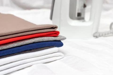 A stack of multicolored clothes close up with the white modern electrical iro Stock Photos