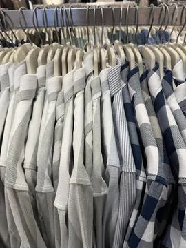 Stack of neatly arranged checkered and striped shirts on hangers in retail .. Stock Photos