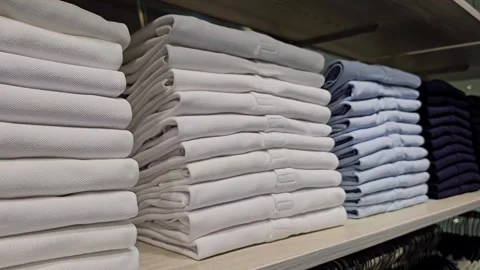 Stack of neatly folded white and light blue polo shirts on wooden shelf in store Stock Footage 313149089
