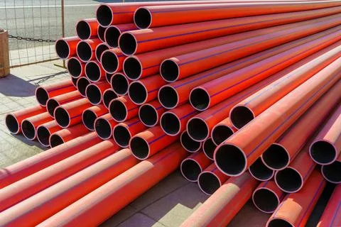 Stack of new, red, plastic, even, long pipelines. PE, HDPE tubes. Stock Photos