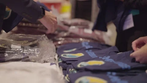 A stack of new T-shirts, some bagged, some open, are presented on a table Stock Footage 257768559