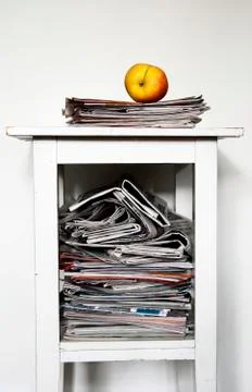 Stack of newspapers on the nightstand and an apple Stock Photos