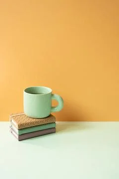 Stack of notebook and mug cup on mint green desk. orange background Stock Photos